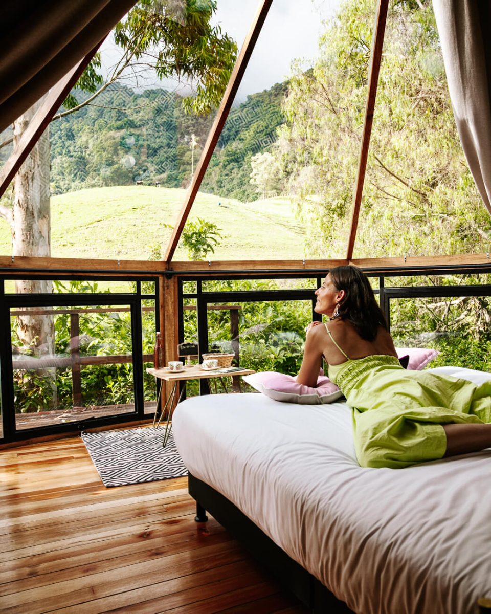 Deborah on bed in tent at Lumbre glamping near Salento in Colombia, with view of surroundings
