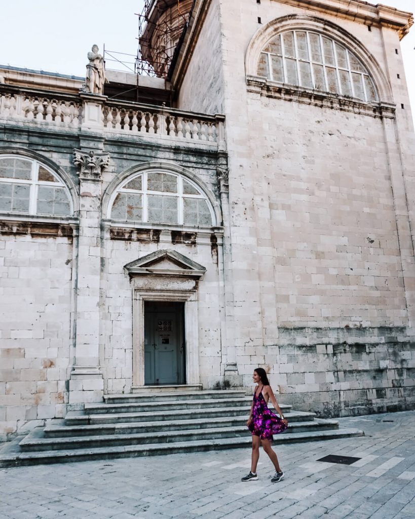 woman on square in Dubrovnik - Dubrovnik is one of the places you will visit with a sail croatia cruise. It is a city you want to discover because of its ancient city walls, baroque buildings, limestone streets and views of the Adriatic sea. But be prepared, as it can be extremely crowded in high season.