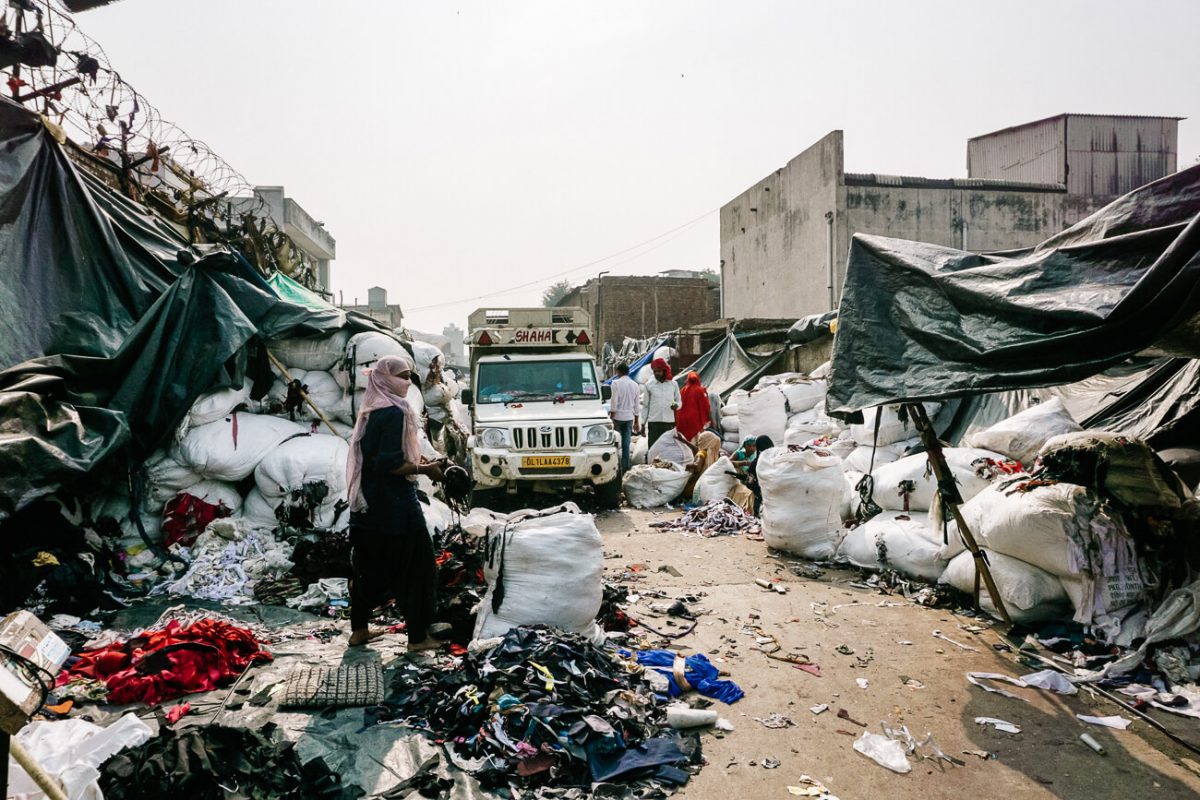 In de kleding recycling straat in Sanjay Colony zijn verschillende kleine bedrijfjes gevestigd, die elk verantwoordelijk zijn voor grote stapels gedragen kleding.